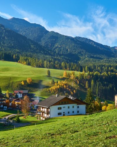 Amazing autumn scenery in Santa Maddalena village with church, colorful trees and meadows under rising sun rays. Dolomite Alps, South Tyrol, Italy.